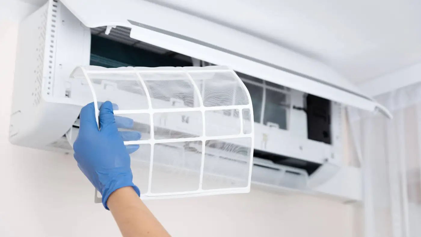 AC filter cleaning in Bristol Gloved hand removing the filter from a wall-mounted air conditioning unit in Bristol