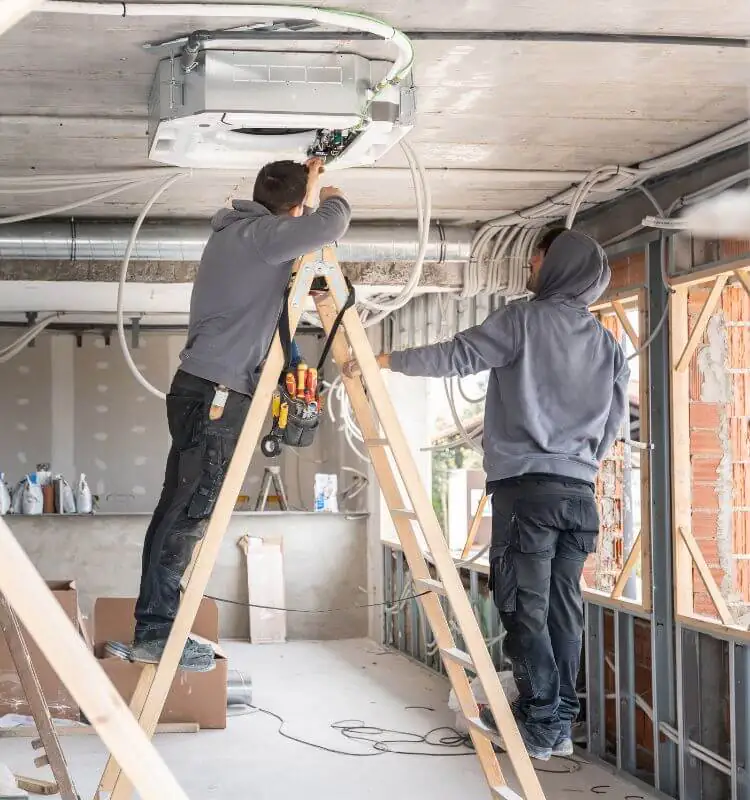 Commercial air conditioning installation in Bristol Two engineers on ladders fitting air conditioning pipework in a commercial unit in Bristol